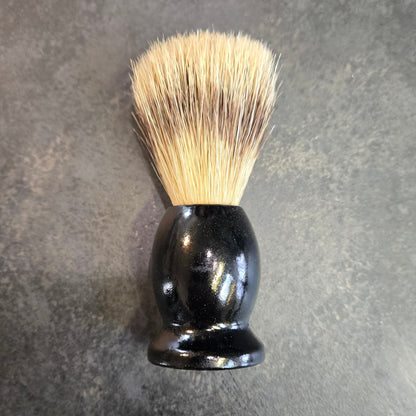Shaving brush with black handle and bristles on a gray surface